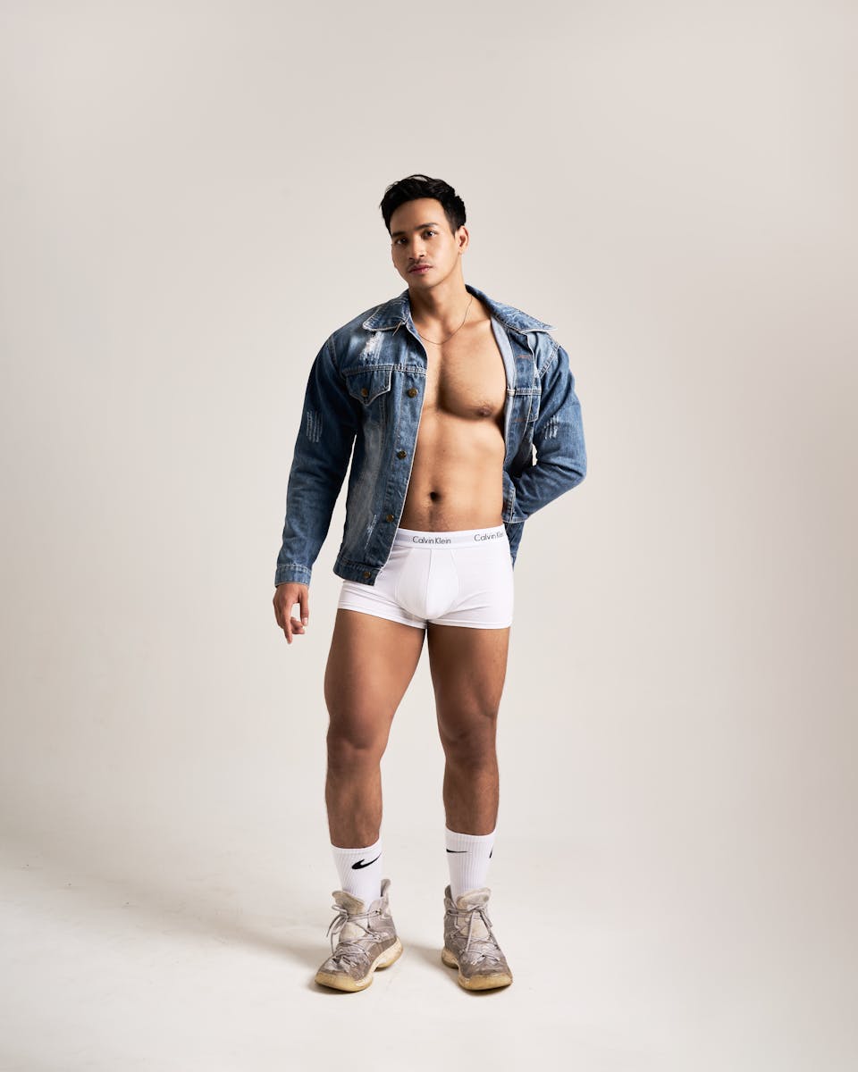 A fashionable male model wearing a denim jacket and white underwear, posing confidently.